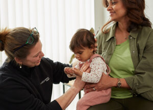 young, at ease toddler being held by her mother as a practitioner chats and performs gentle mobility tests