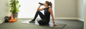 athletic-looking female patient sits on a yoga mat drinking from a water bottle