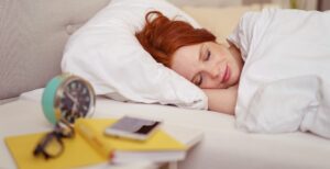 Woman sleeping in bed with a serene smile on her face and an alarm clock on the table alongside